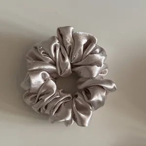 Detail van een champagnekleurige satijnen scrunchie met kleine strass accenten.