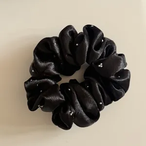 Detailopname van een zwarte satijnen scrunchie met glimmende zilveren strassteentjes