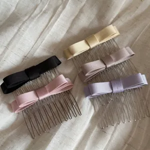 Detail shot of five satin bow hair combs in elegant pastel colors on white fabric.