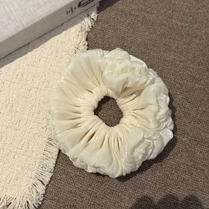 Close-up van een crème satijnen scrunchie met zachte parelmoerachtige geplooide textuur