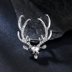 Close-up of silver deer head brooch with sparkling rhinestone antlers on a dark rock.