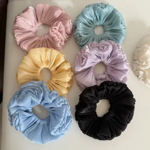 Detailed view of pleated shimmering fabric scrunchies in various pastel colors
