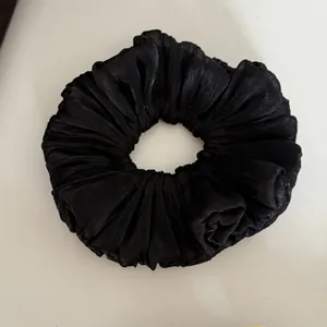 Close-up detail of a large black pleated hair scrunchie with soft flowing texture