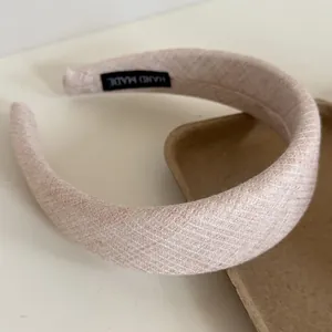 Detailed view of a wide cream-colored linen headband with a Hand Made tag inside.