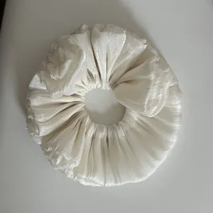 Close-up detail of a cream shimmering pleated oversized hair scrunchie with soft ruffled texture.