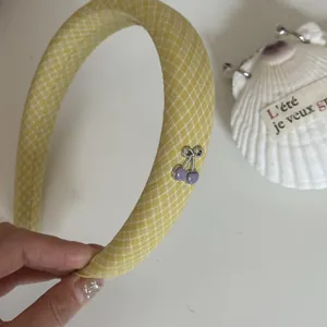 Detalle de diadema de tela a cuadros amarillos con dije de cereza morada.