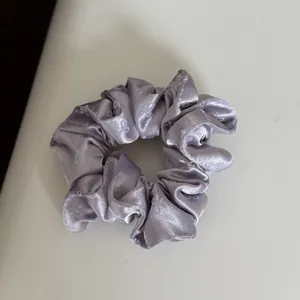 Detail macro view of a lavender satin scrunchie featuring a white bow pattern design.