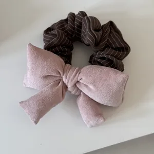 Detail of dusty pink suede bow and brown striped elastic hair scrunchie accessory.