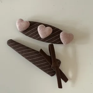 Close-up detail of stylish brown fabric hair clips featuring pink plush hearts and a ribbon bow
