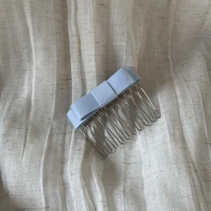 Close-up of an elegant light blue satin bow hair comb placed on a textured beige linen fabric