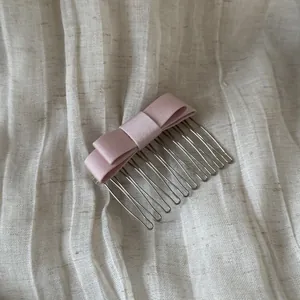 Macro view of a soft pink satin bow hair comb placed on a textured linen fabric.