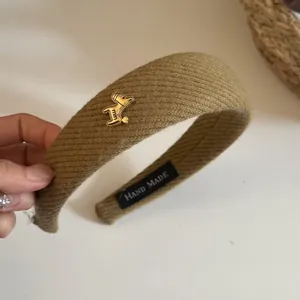 Close-up detail of a khaki twill wide headband featuring a gold pony charm and label.