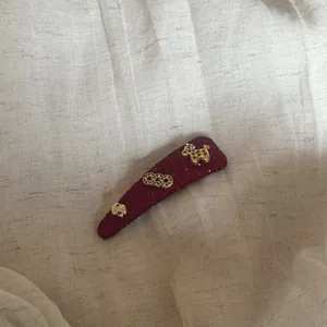 Detailopname van de bordeauxrode haarspeld met goudkleurige paarden- en muntbedeltjes.