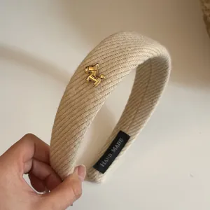 Close-up detail of a beige ribbed fabric wide headband with a cute golden horse charm