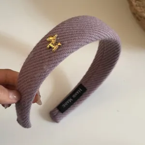 Detail view of purple ribbed wide headband with elegant golden horse charm and handmade label