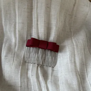 Detailed view of a dark red satin bow hair comb on white textured linen fabric.