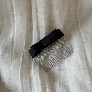 Close-up detail of a minimalist black satin bow hair comb with polished metal teeth