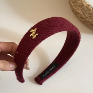 Detail of a burgundy ribbed knit headband with a golden horse charm and handmade label.