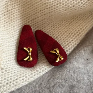 Pinzas de pelo de tela a cuadros rojos con lazos dorados, vista detallada de cerca.