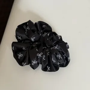 Detailed view of a black satin scrunchie with white bow patterns on white surface