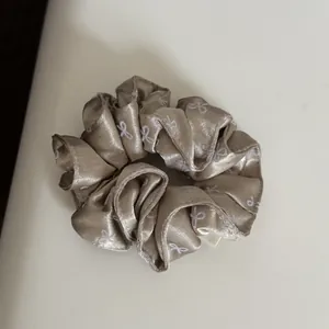 Detail view of a champagne satin scrunchie featuring elegant white bow patterns