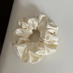 Close-up detail of a cream-colored ruffled satin hair scrunchie with soft sheen