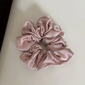 Close-up of rose pink satin scrunchie featuring elegant white bow embroidery details