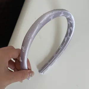Close-up of a lavender satin headband featuring delicate white bow pattern designs