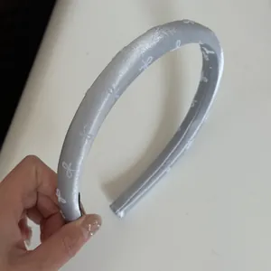 Close-up detail of silver-grey satin headband featuring elegant white bow patterns