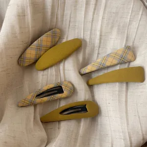 Vue détaillée des barrettes BB en tissu jaune à carreaux et uni sur un fond en lin