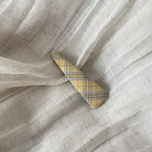 Gros plan d'une pince à cheveux à carreaux jaune gingembre sur tissu de lin fin
