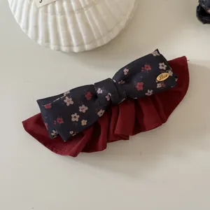Detail shot of a vintage floral bow hair clip with dark red ruffled fabric accents.