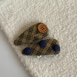 Close-up detail of two plaid fabric hair clips with wooden button and handmade tag