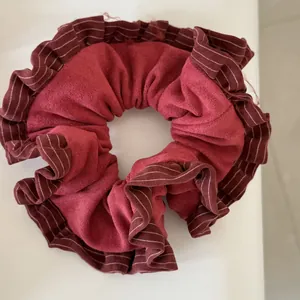 Close-up detail of a wine red suede scrunchie featuring elegant striped ruffled edges.