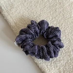 Macro detail of a vintage purple plaid fabric scrunchie on cream textured background