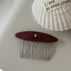 Close-up of a burgundy striped hair comb featuring a delicate red bow accessory.