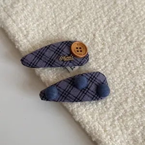 Close-up of two purple plaid fabric hair clips with button and ball accents on white fleece.