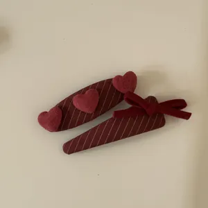 Detail view of burgundy striped hair clips featuring plush hearts and a velvet bow decoration
