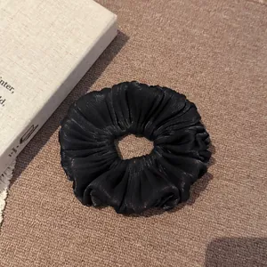Macro-overzicht van een zwarte satijnen geplooide scrunchie met een parelmoer glans