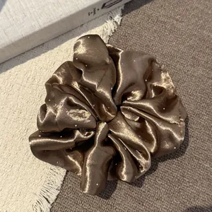 Detailweergave van bruine satijnen scrunchie met fonkelende sterrenbeeld strass steentjes