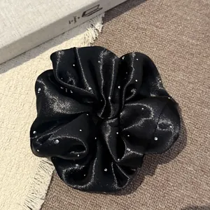 Detailweergave van zwarte parelmoer satijnen scrunchie met fonkelende ster-strass-steentjes
