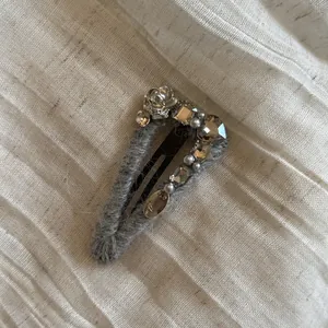 Vue détaillée d'une pince à cheveux grise ornée de strass et de perles.