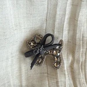 Détail d'une pince à cheveux petit chien gris en strass scintillants avec un nœud noir élégant