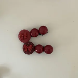 Detailed view of two wine red hair clips with glossy beads and bow accents