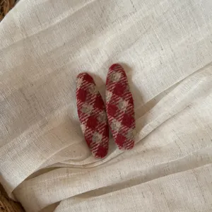 Detailopname van twee rood geruite stoffen haarspelden op een zachte beige linnen stof