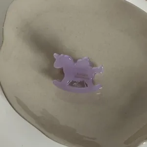 Gros plan d'une pince à cheveux en acétate violette en forme de cheval à bascule.