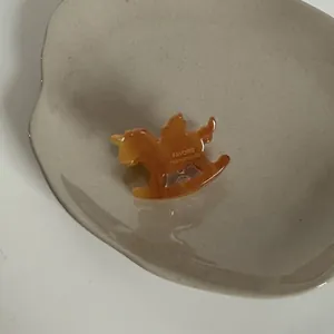 Détail montrant la texture en acétate ambré et le design de cheval à bascule du clip