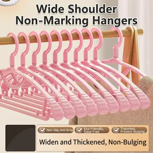 Set of pink wide-shoulder seamless plastic clothes hangers hanging on a wooden garment rack
