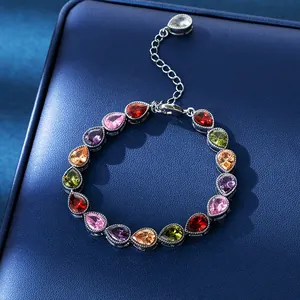 Close-up of elegant teardrop zircon bracelet with colorful stones on blue leather background.