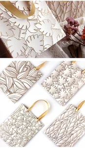 Detailansicht weißer Geschenktüten mit glitzerndem Blattmuster und goldenen Bändern.
